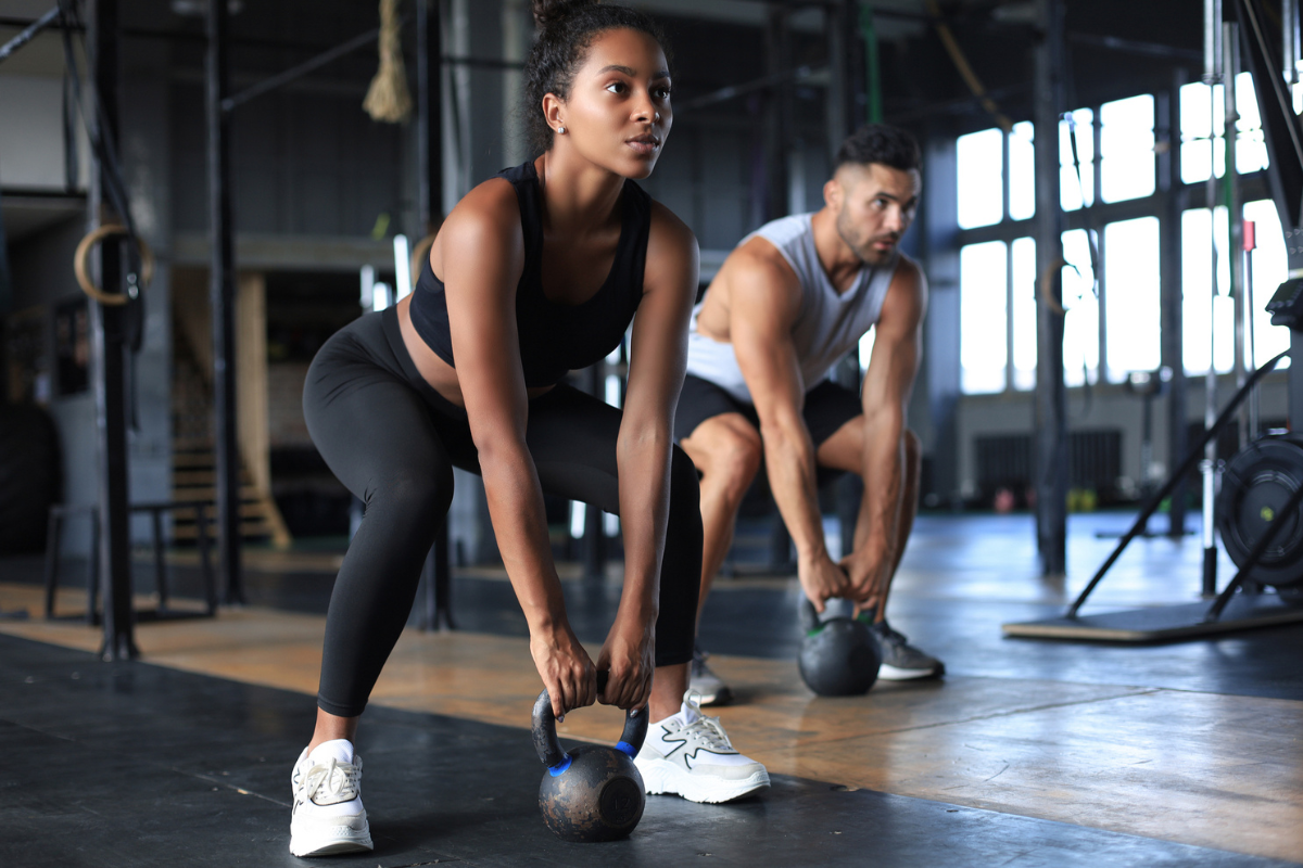 woman and man in large gym doing kettlebells